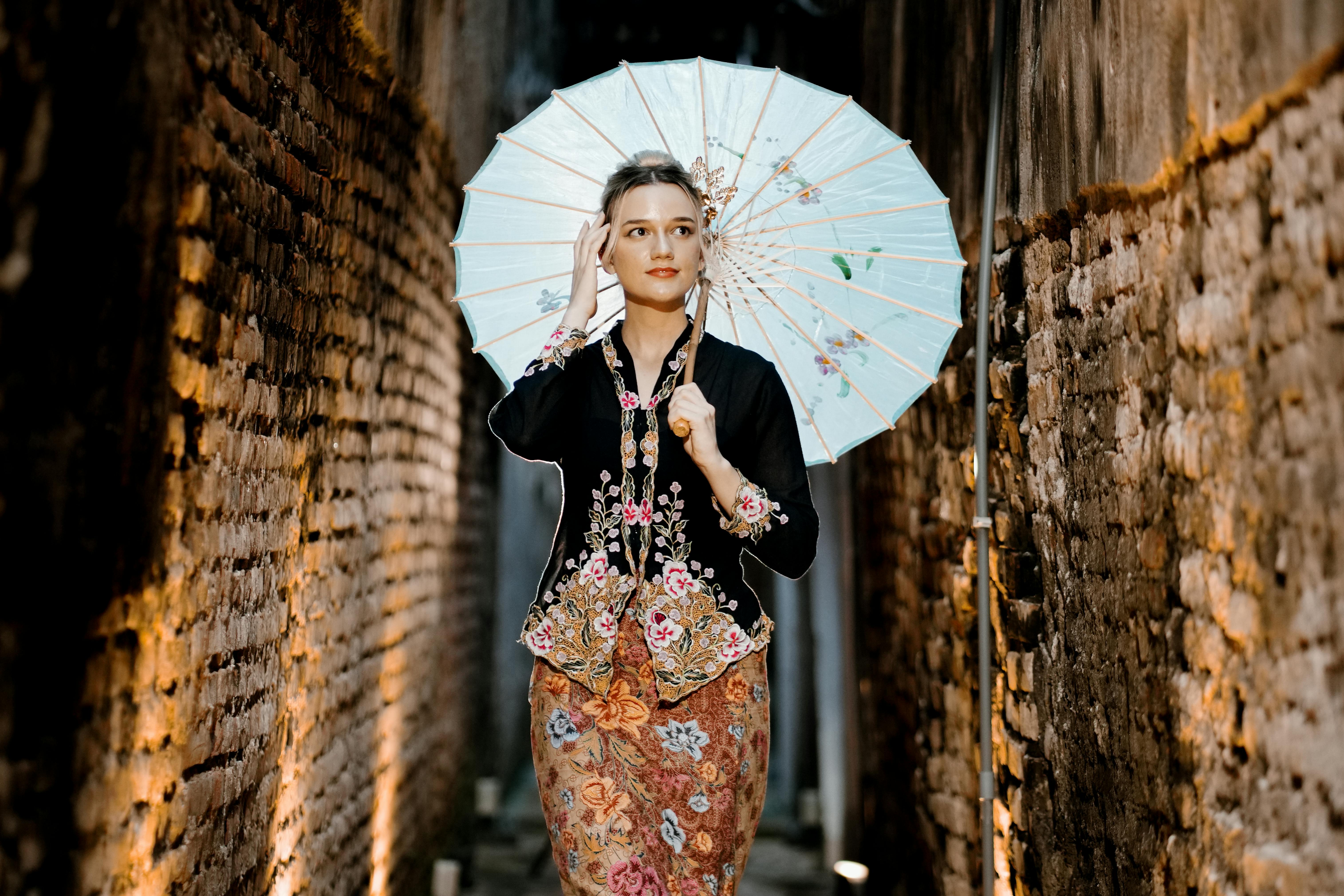 Woman in traditional kebaya dress holding a parasol in a narrow, atmospheric alley.