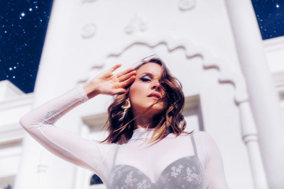 Stunning fashion portrait of a woman posing gracefully against a historic Los Angeles landmark under a starry sky.