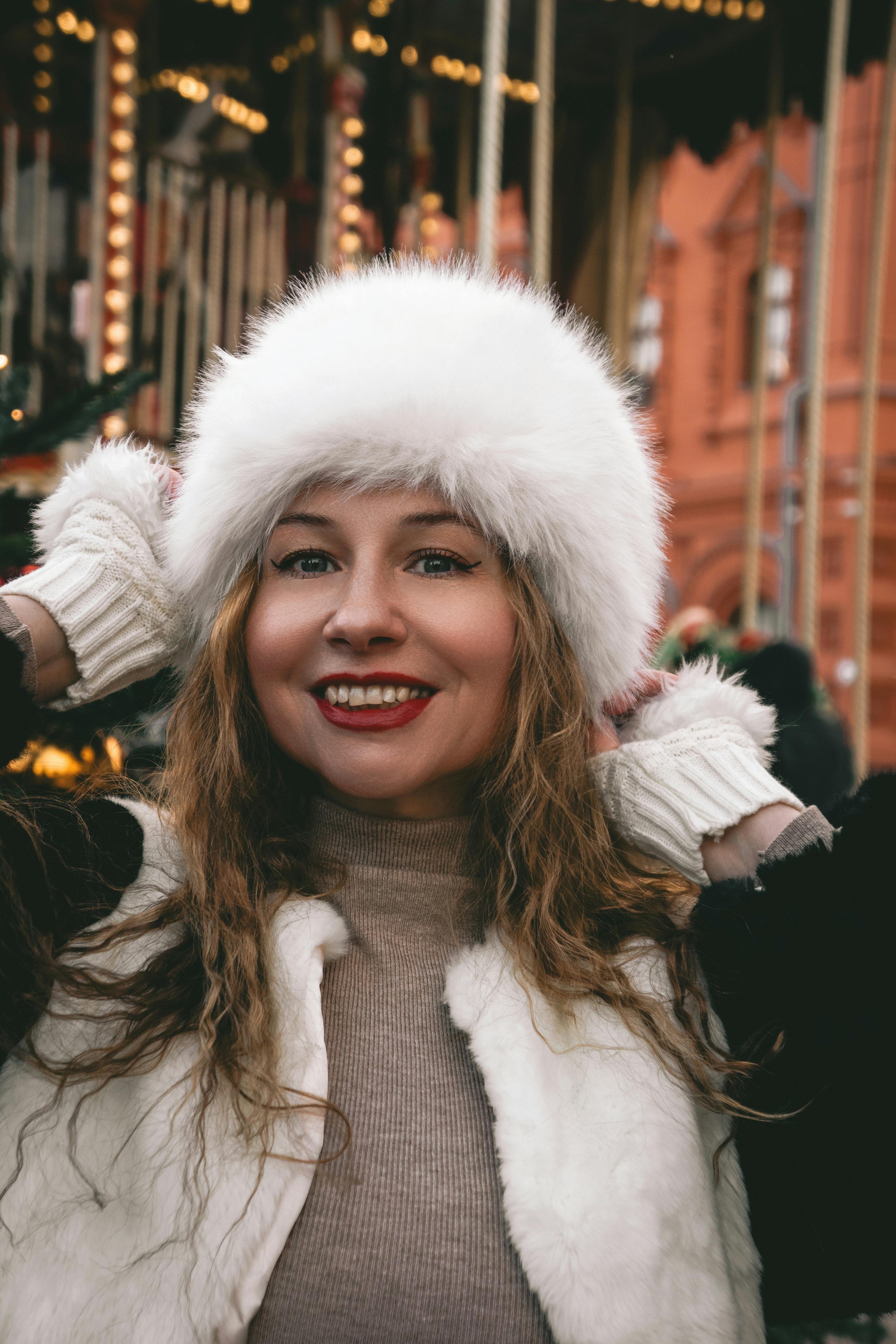 Happy woman in white fur hat and gloves enjoying winter outdoors.
