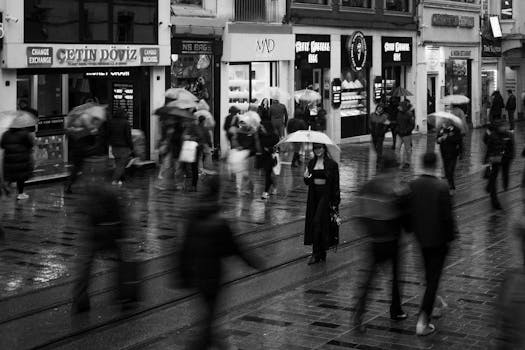Black and white scene of people with umbrellas on İstiklal Street, Istanbul during rain.
