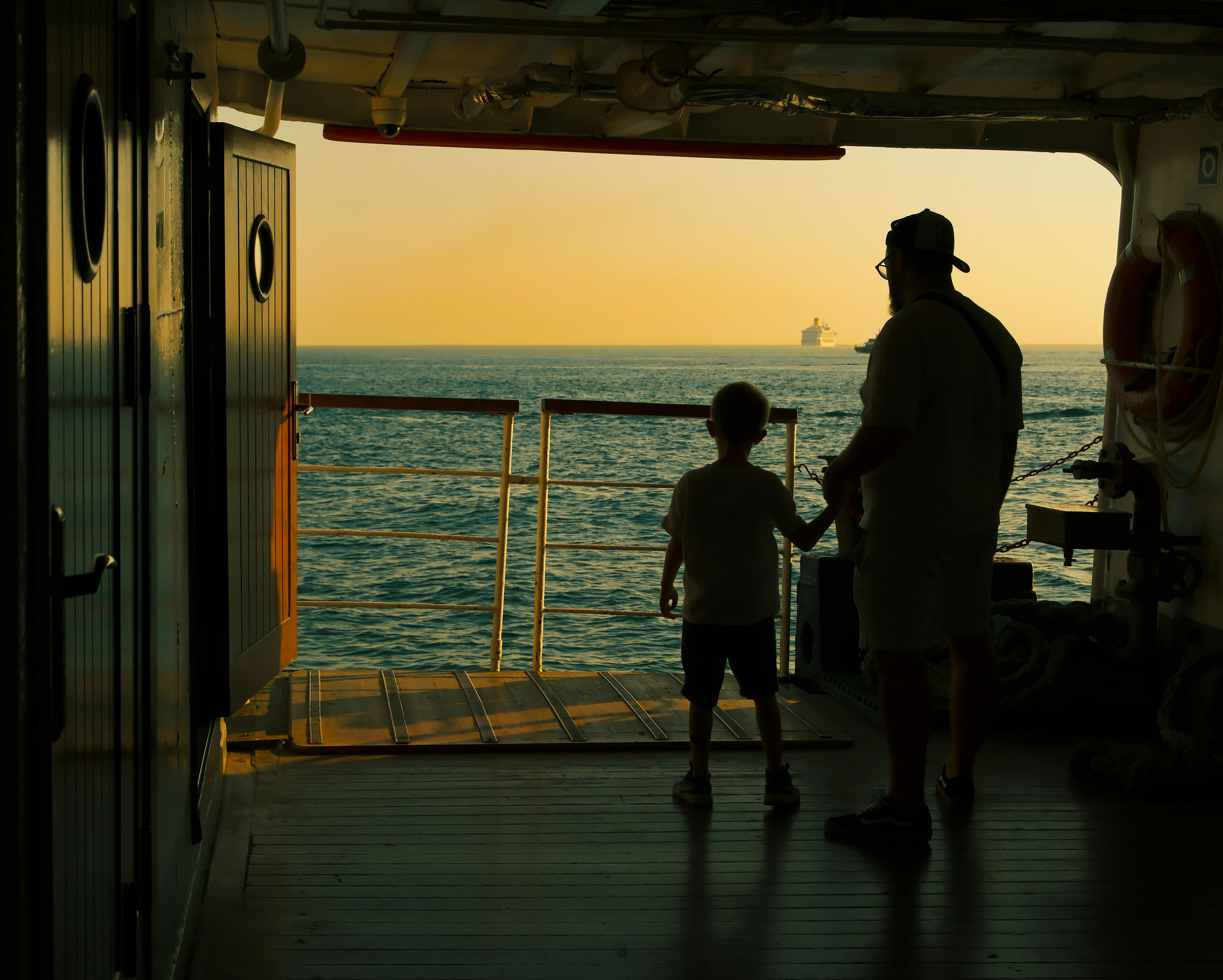 A silhouette of a father and son enjoying a serene ocean view from a ship deck.