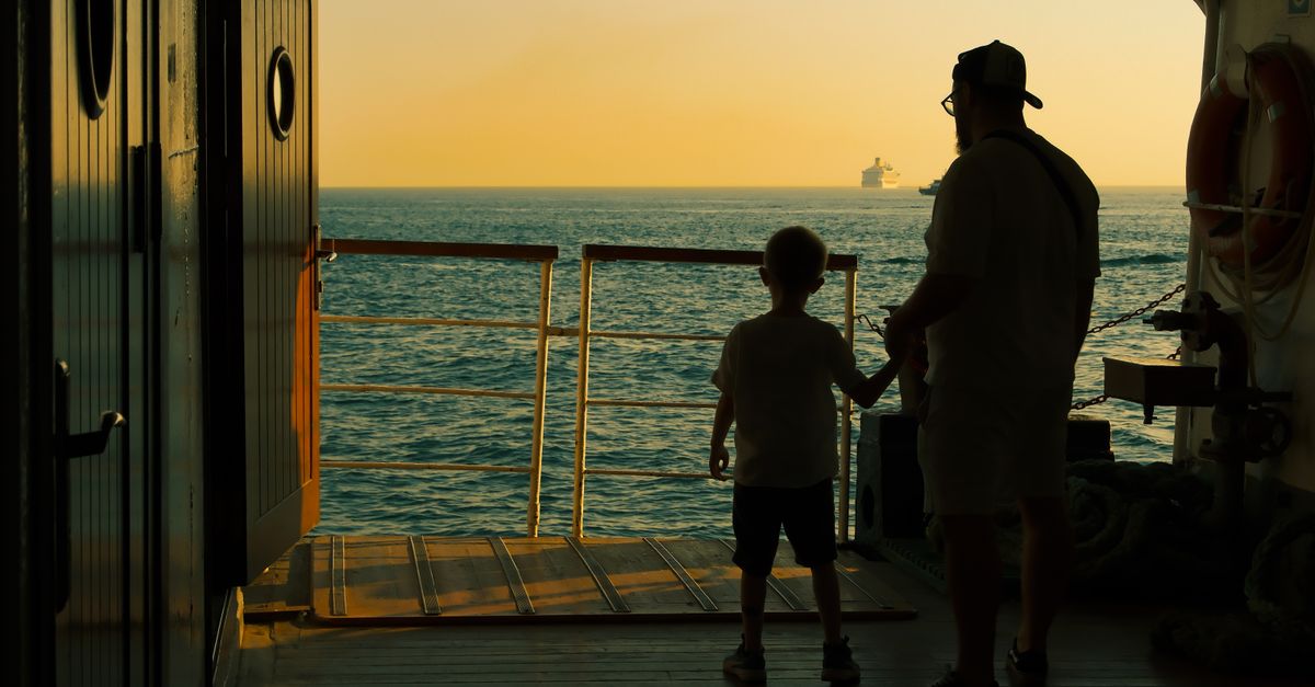A silhouette of a father and son enjoying a serene ocean view from a ship deck.