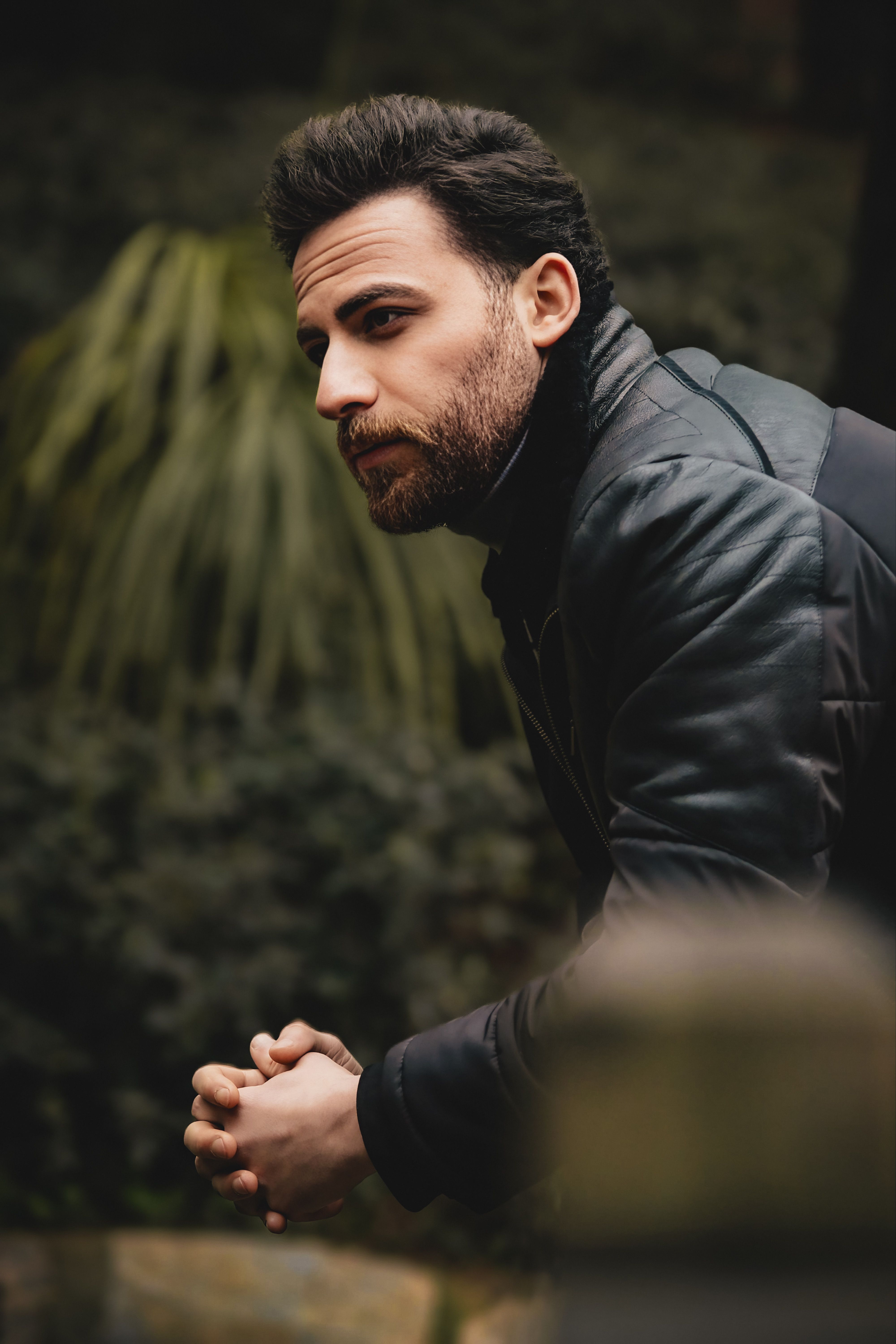 Thoughtful man leaning outdoors surrounded by greenery, deep in contemplation.