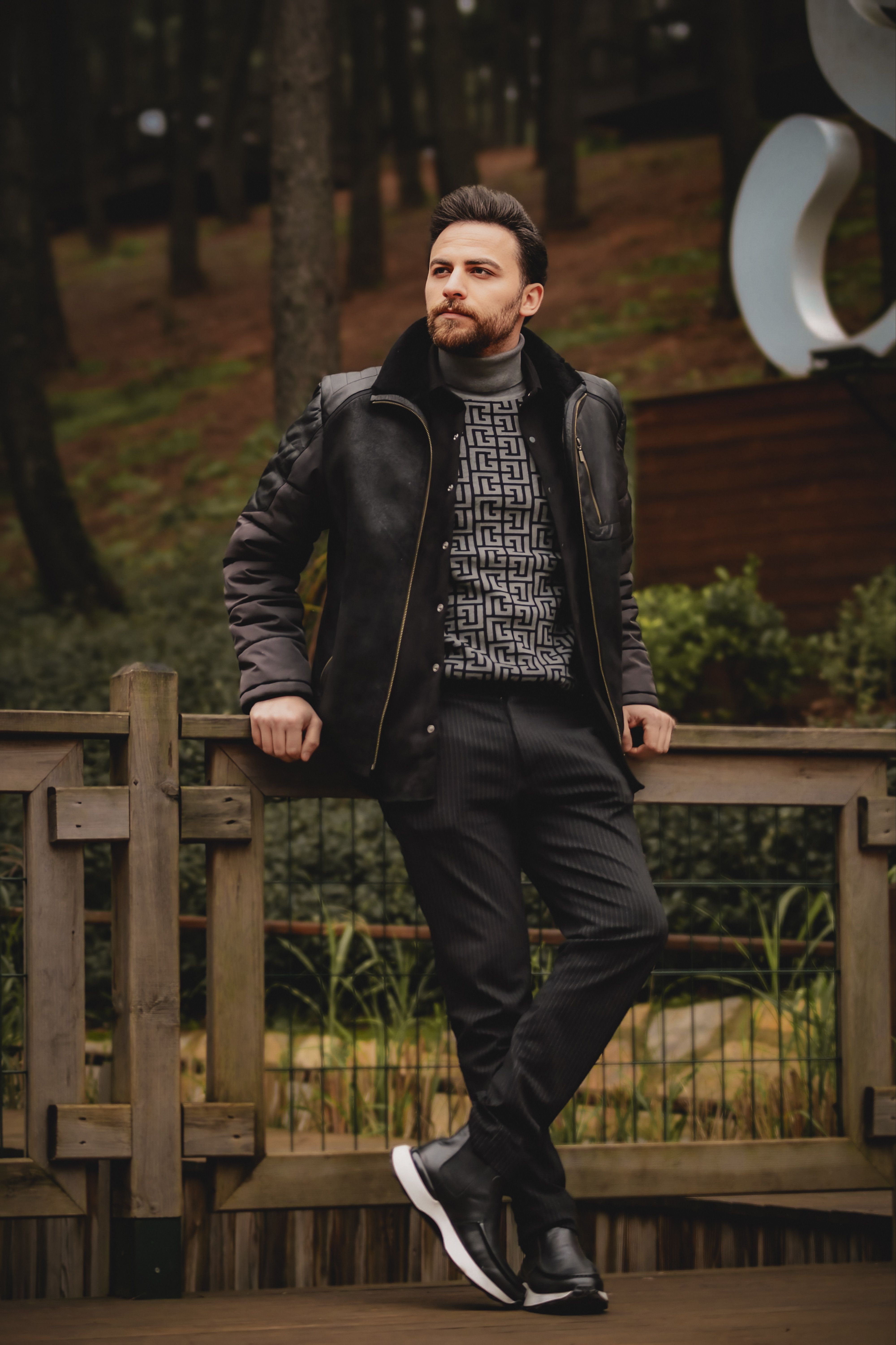 Stylish man in a jacket and sneakers posing outdoors, showcasing modern fashion.