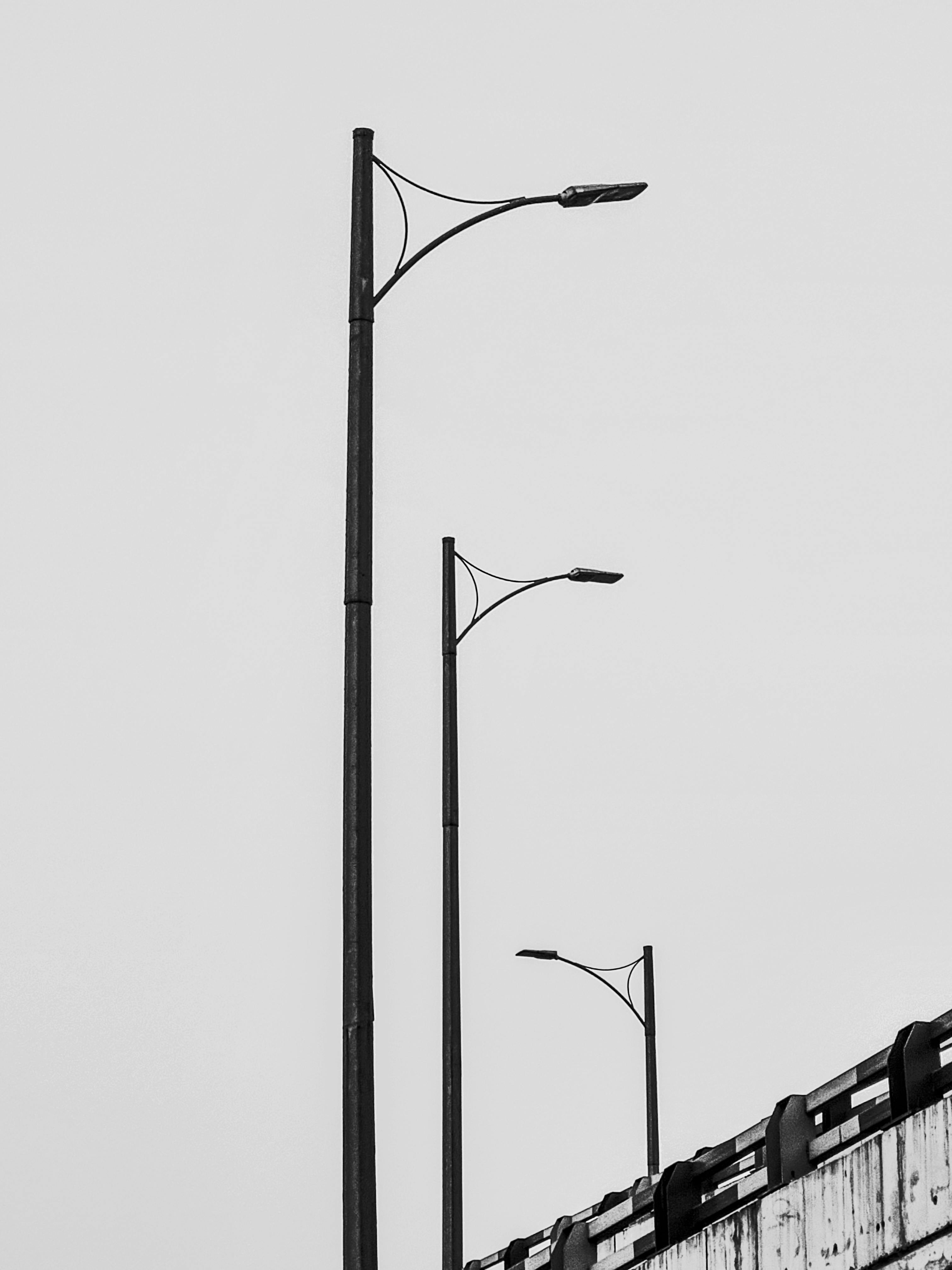 Gratuit Photo minimaliste en noir et blanc de lampadaires sur un pont, avec un ciel dégagé en arrière-plan. Photos