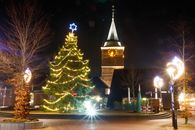 Illuminated Christmas tree and church under a starry night sky, exuding holiday spirit.