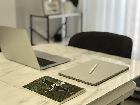 Modern minimalist office desk setup with a laptop, tablet, and book on a marble table.