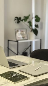 A clean, modern workspace featuring a laptop, notebook, and plant on a marble table.