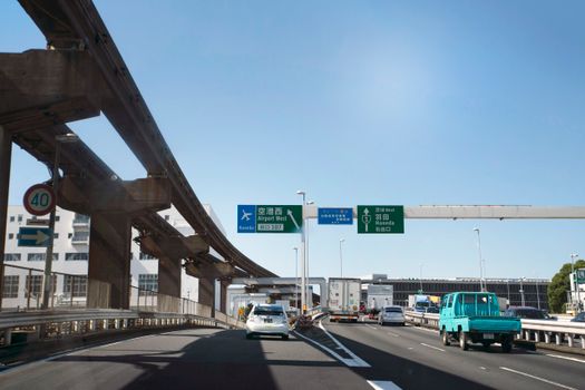 Cars on highway with signs towards Haneda Airport on a clear day in Tokyo.