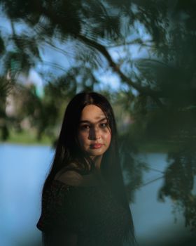 A contemplative woman surrounded by lush greenery by a tranquil lake.