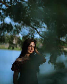 Portrait of a woman surrounded by lush greenery near a tranquil lake.