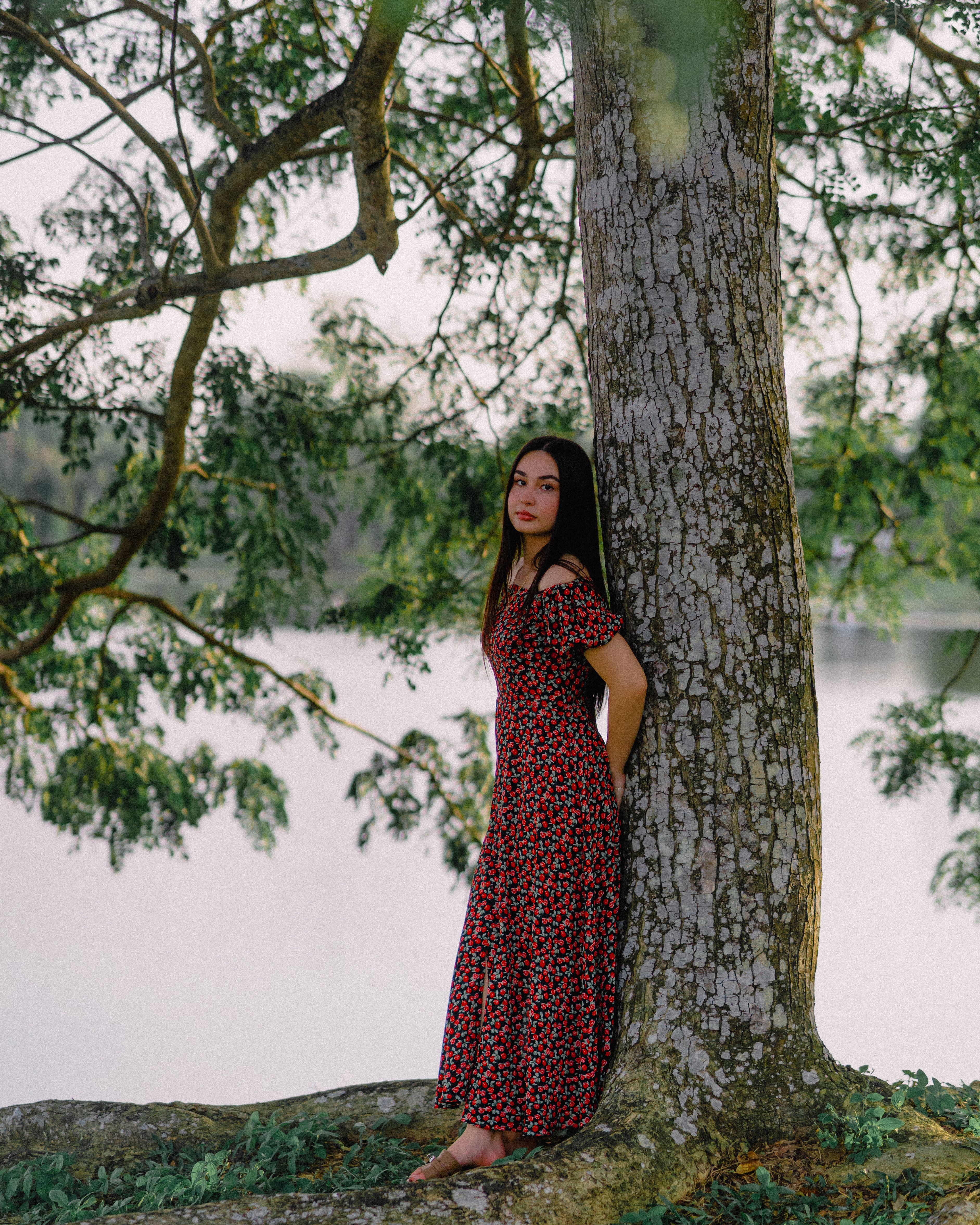 Woman in floral dress leaning against tree by a lake · Free Stock Photo