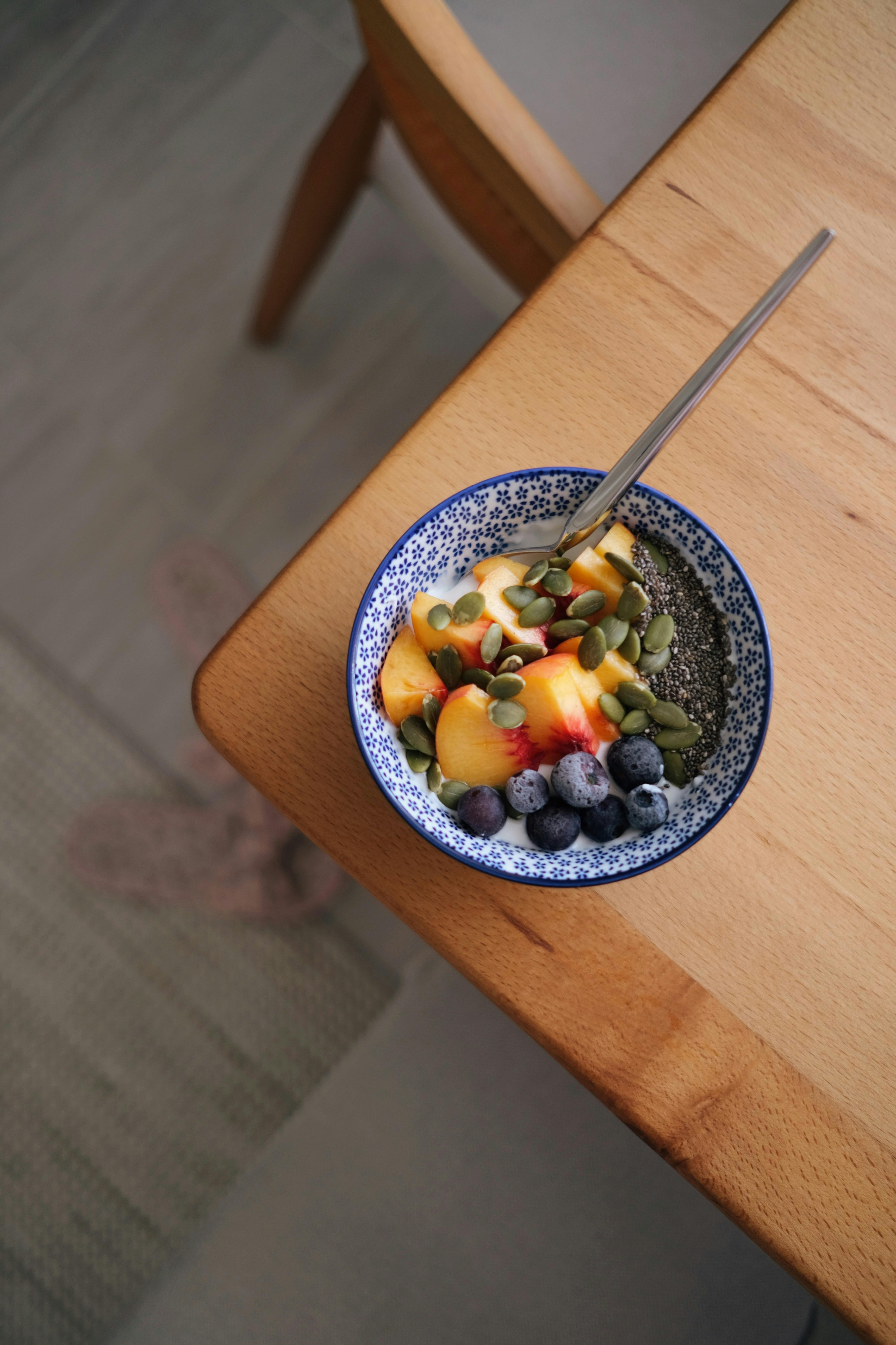 Top down view of a vibrant breakfast bowl with chia seeds, blueberries, peaches, and pumpkin seeds on a wooden table.