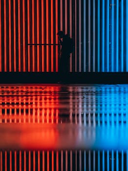 Silhouetted person stands against a striking backdrop of red and blue neon lighting with reflections.