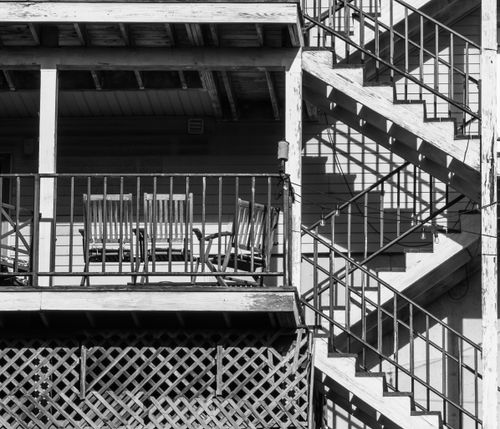 Free Black and white photo of a fire escape and chairs on a balcony. Stock Photo
