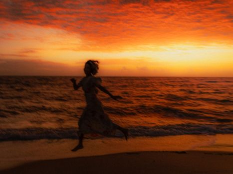 A woman silhouetted against a vibrant sunset, running along the beach with a dramatic red sky.