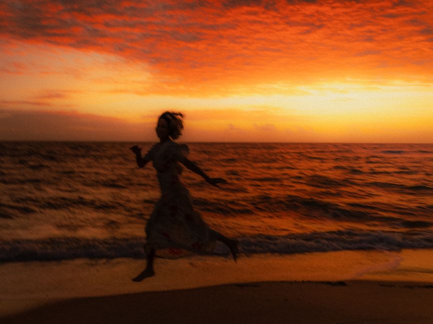 A woman silhouetted against a vibrant sunset, running along the beach with a dramatic red sky.