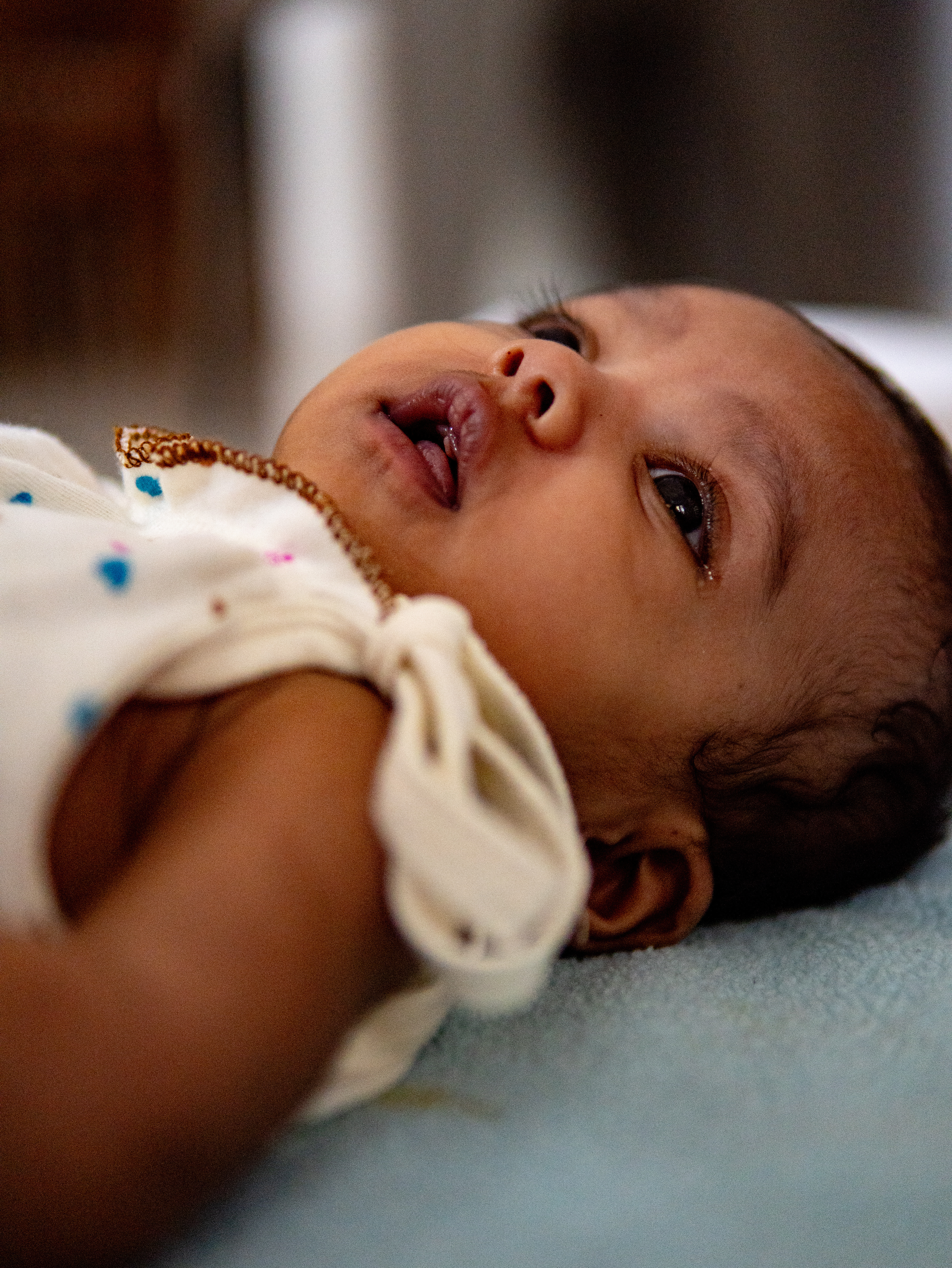 Close-up of a cute baby lying on a blanket with a curious expression indoors.