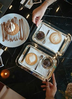 Stylish cafe table with cappuccinos and a dessert adorned with chocolate sauce.