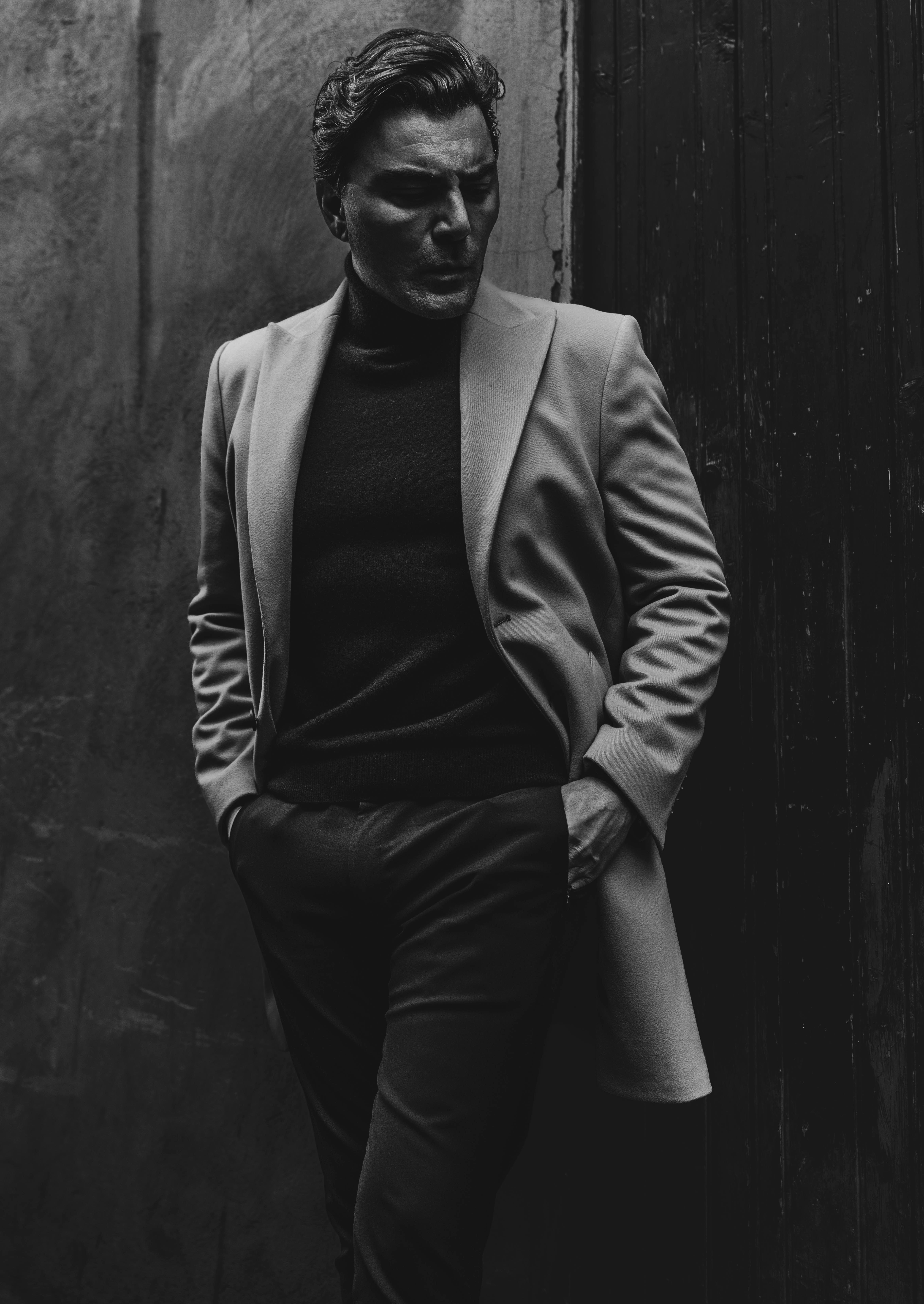 Stylish man in coat leaning against wall, capturing elegance.