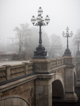 Moody winter morning on a historic bridge with fog and street lamps in Hamburg.