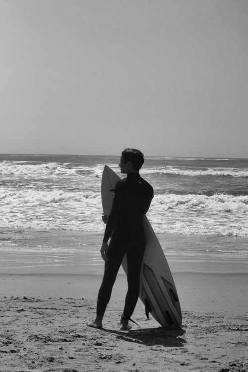 Free Silhouette of a surfer with a surfboard gazing at the ocean waves on a beach. Stock Photo