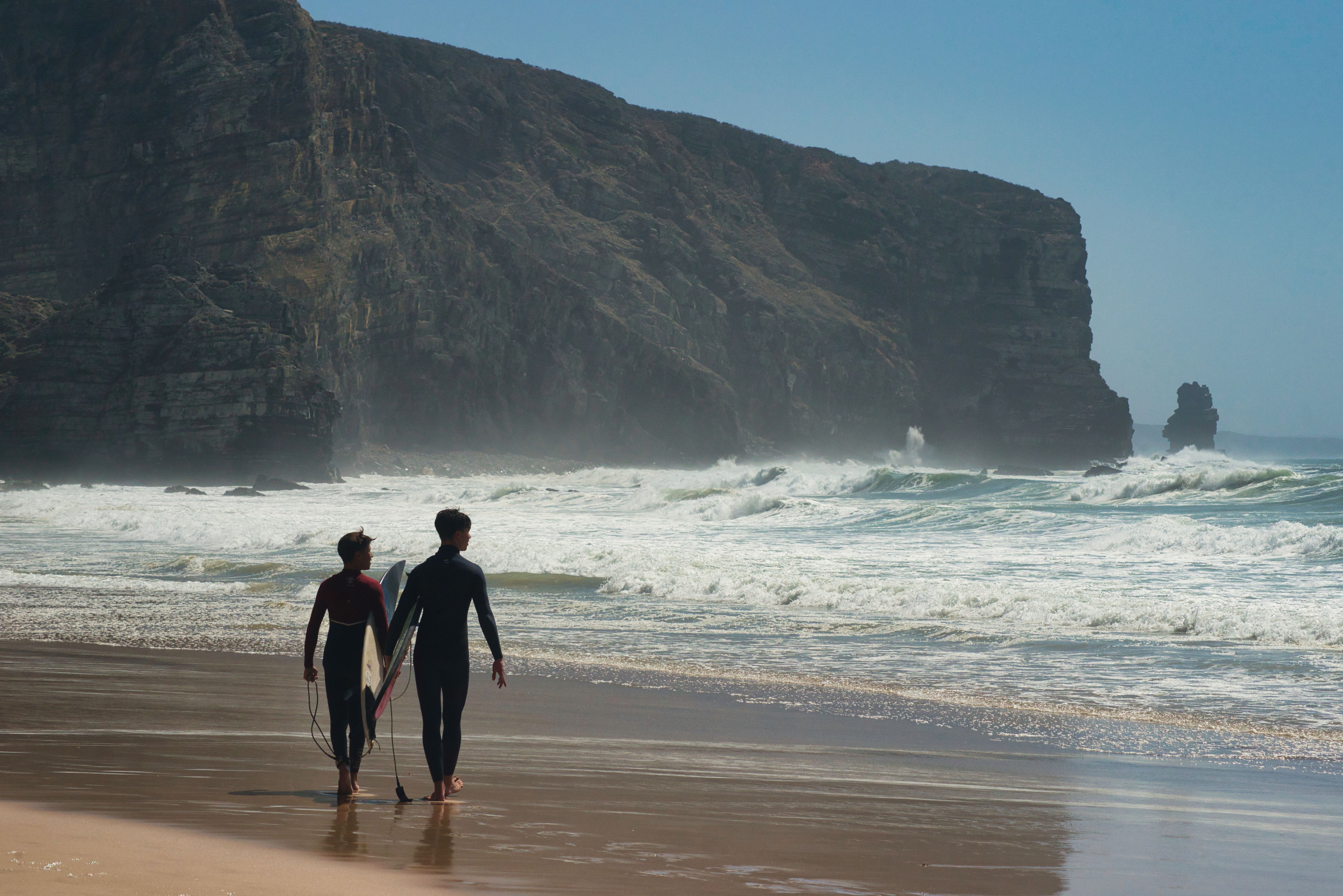 Surfers in the water at Ribeira d’Ilhas with the cliff path and cafe above the reef