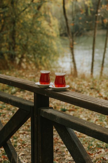 Two glasses of red tea on a wooden railing in a serene outdoor autumn setting by the river.