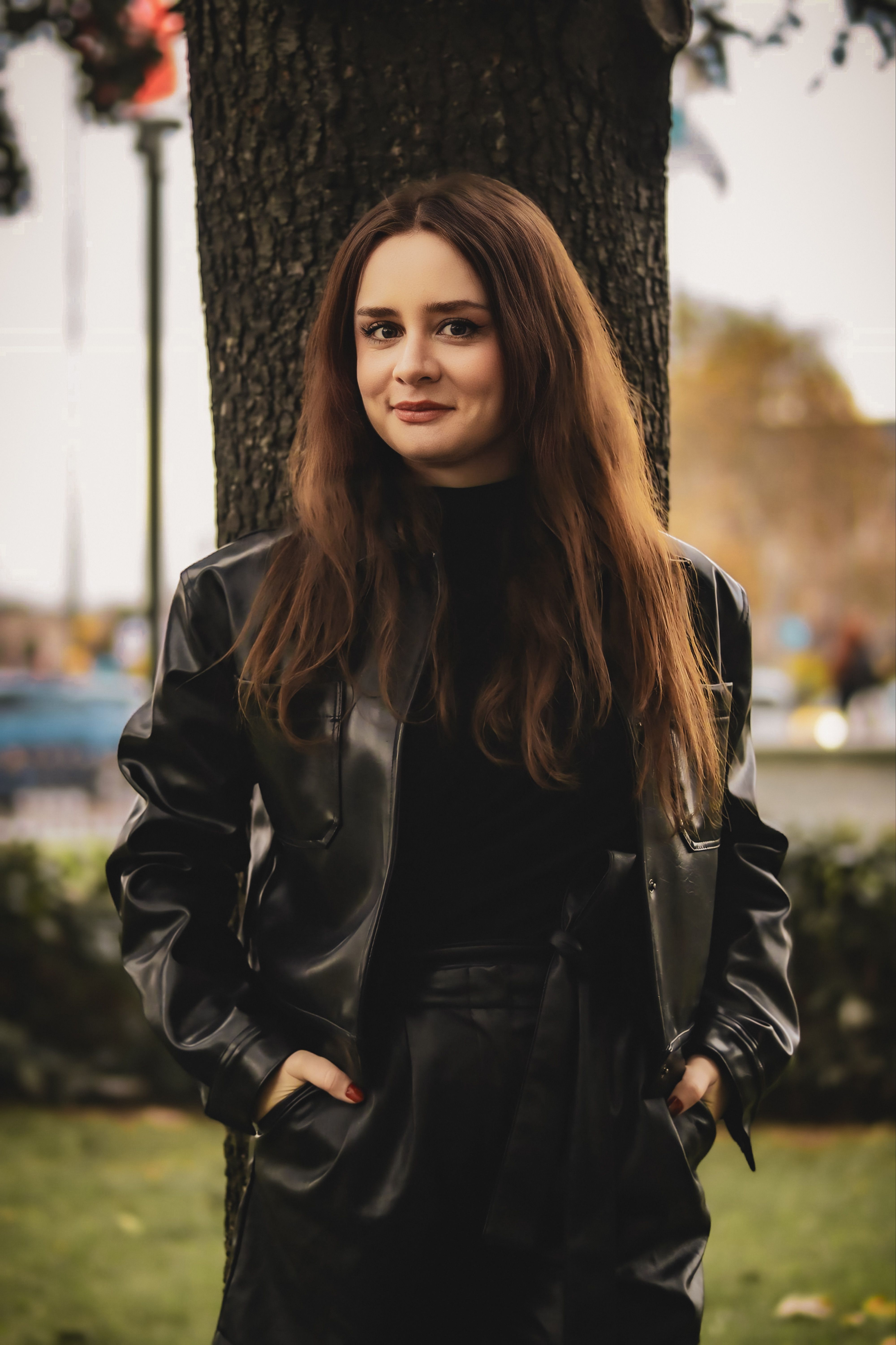 Stylish young woman in a black leather jacket standing outdoors in autumn.