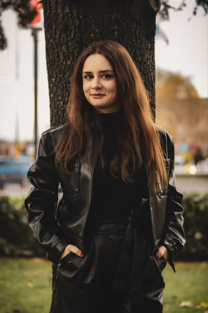 Stylish young woman in a black leather jacket standing outdoors in autumn.
