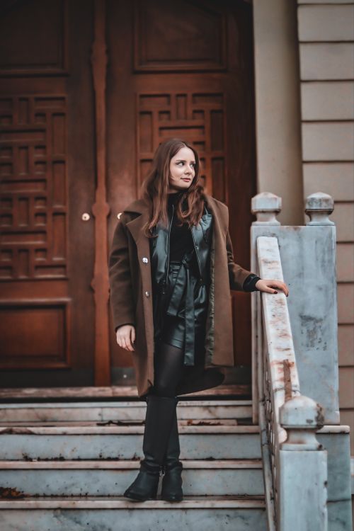 Free A woman stands confidently on marble steps in front of a wooden door, showcasing a chic winter fashion ensemble. Stock Photo
