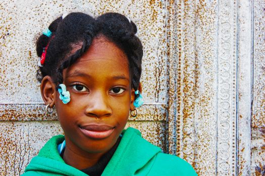 Close-up portrait of a confident young girl with braided hair against a textured wall.