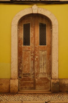 Elegant vintage wooden door set in a yellow wall in Lisbon, showcasing historic architecture.