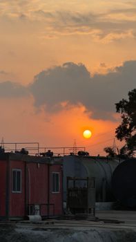 Industrial site with storage tanks at sunset, casting a warm glow in the sky.