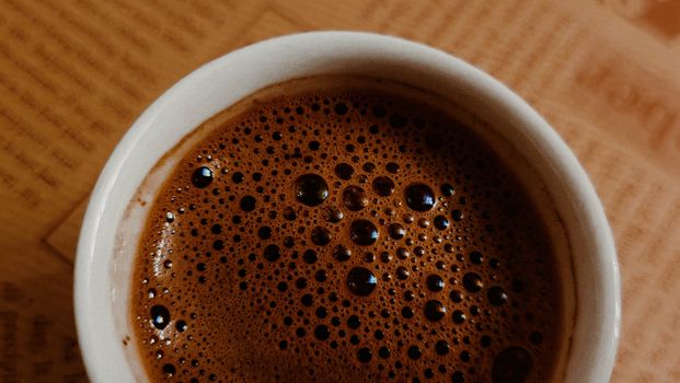 Top view of a coffee cup with rich froth on a newspaper background.