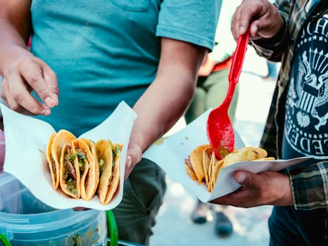 Close-up of street food vendors serving freshly-made tacos with vibrant ingredients at a market.
