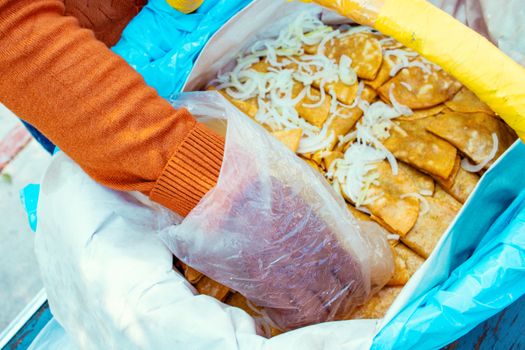 Person retrieving crispy snacks from a plastic bag at an outdoor market.