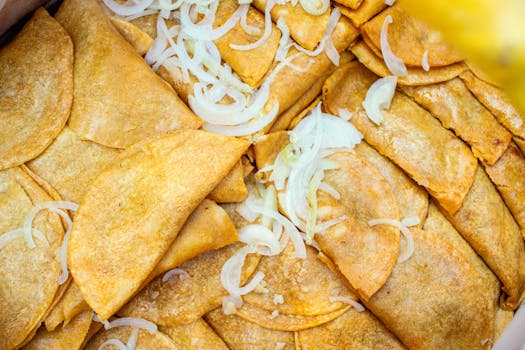 Close-up of golden fried tacos with fresh onion garnish, showcasing a delicious traditional snack.