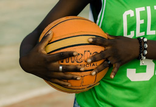 Detailed shot of hands gripping a basketball, wearing a sports jersey outdoors.