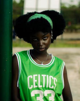 Stylish young woman wearing a Celtics jersey poses outdoors with a confident expression.