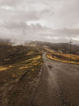 Winding mountain road with dramatic landscape under cloudy skies.
