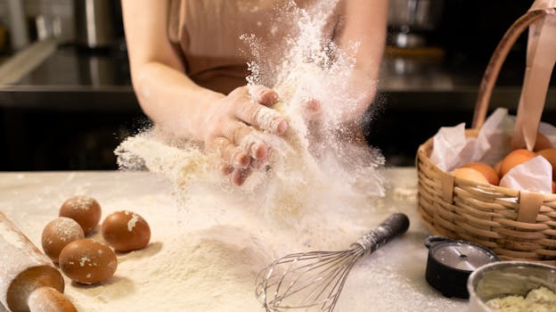 A baker kneads dough surrounded by eggs, flour, and baking tools in a cozy kitchen.