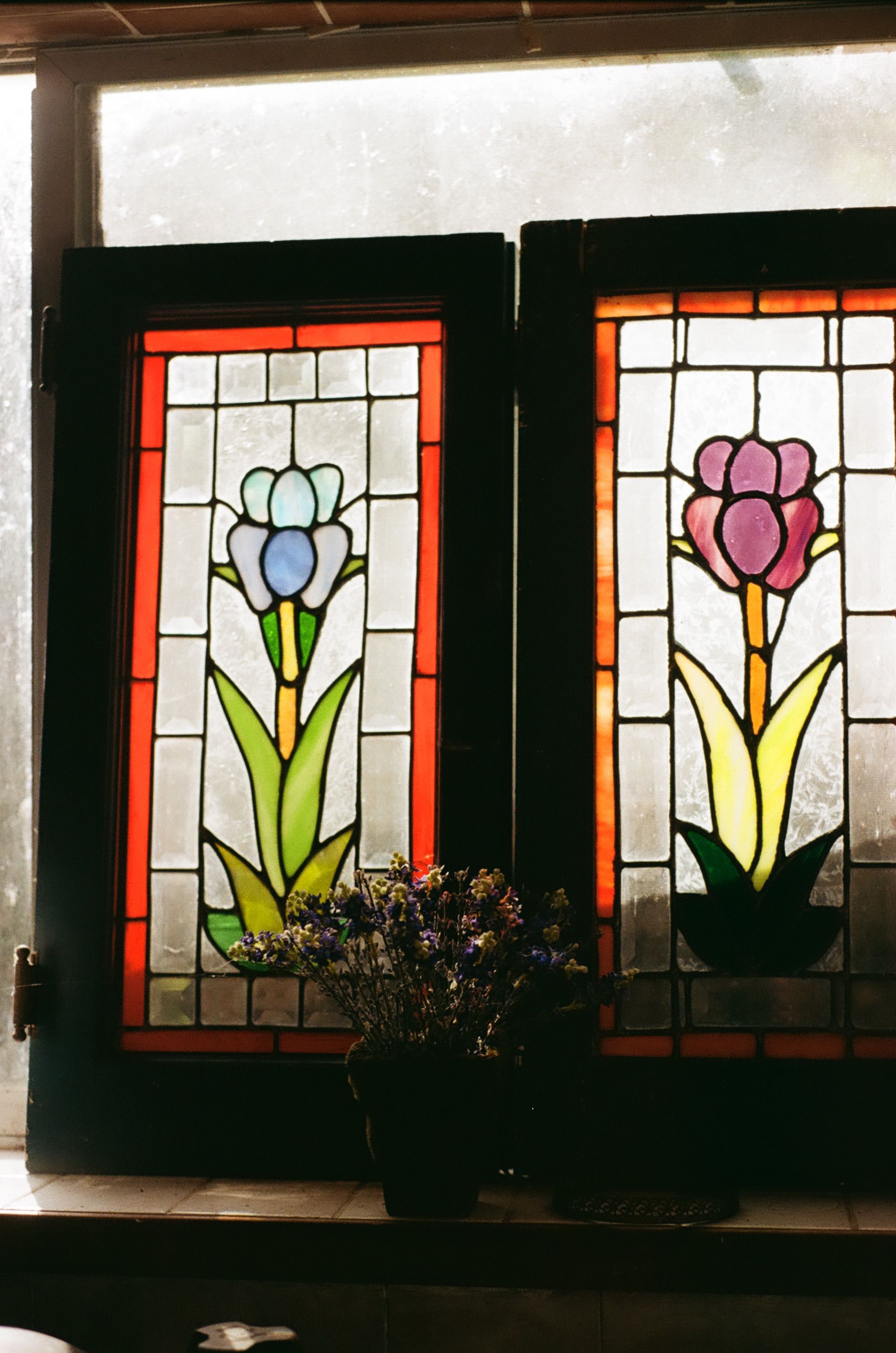 Stained glass windows with vibrant floral design and a vase of flowers for artistic home decor.