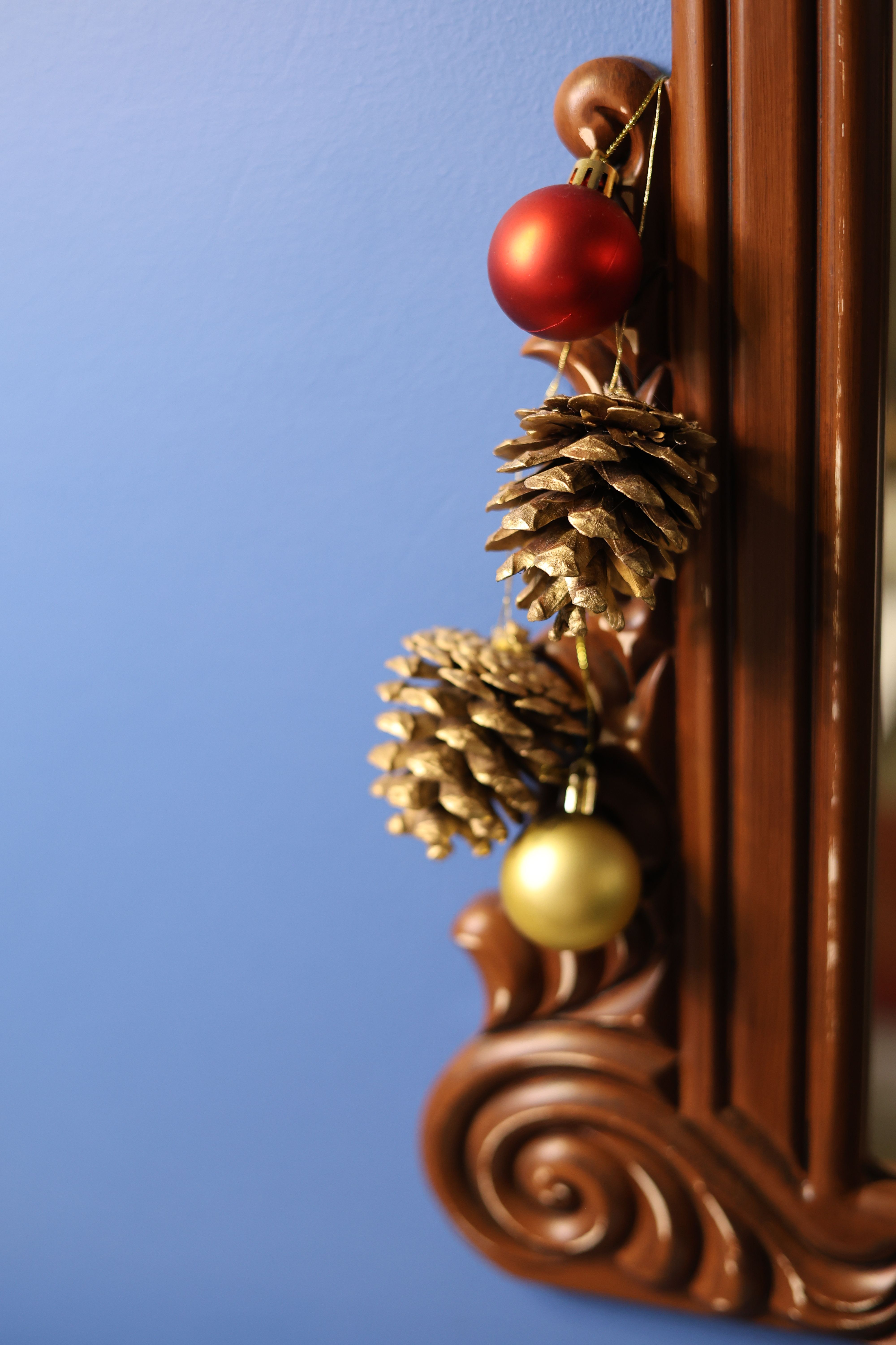 Close-up of holiday pine cones and ornaments on a wooden frame, indoors with a blue background.