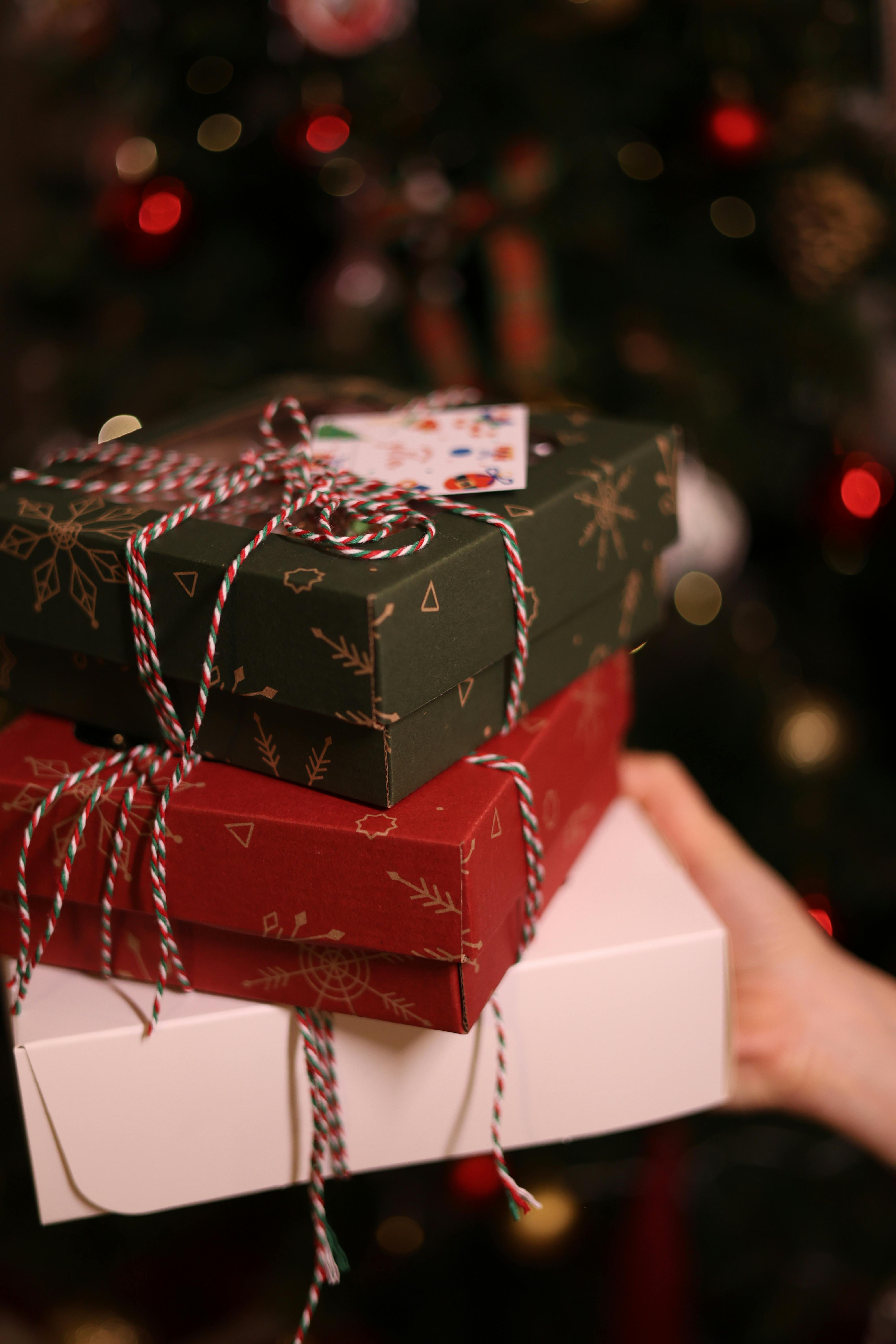 Stack of Christmas gift boxes with twine ribbon in front of a decorated tree.