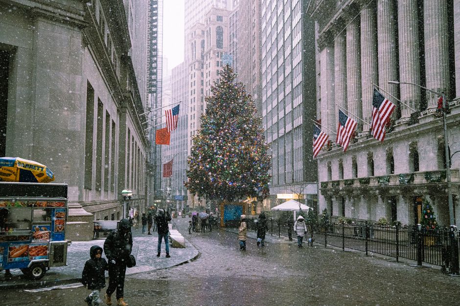 A snowy winter scene in New York City with a decorated Christmas tree and bustling street life.