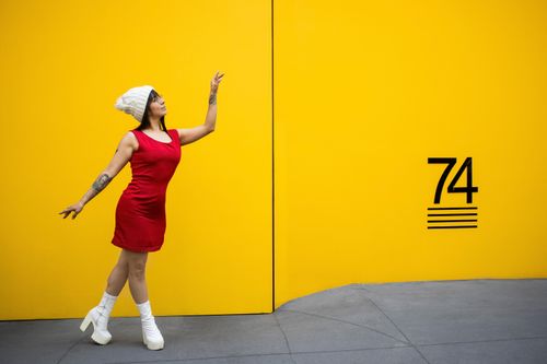 Free A stylish woman in a red dress poses gracefully against a bright yellow wall. Stock Photo