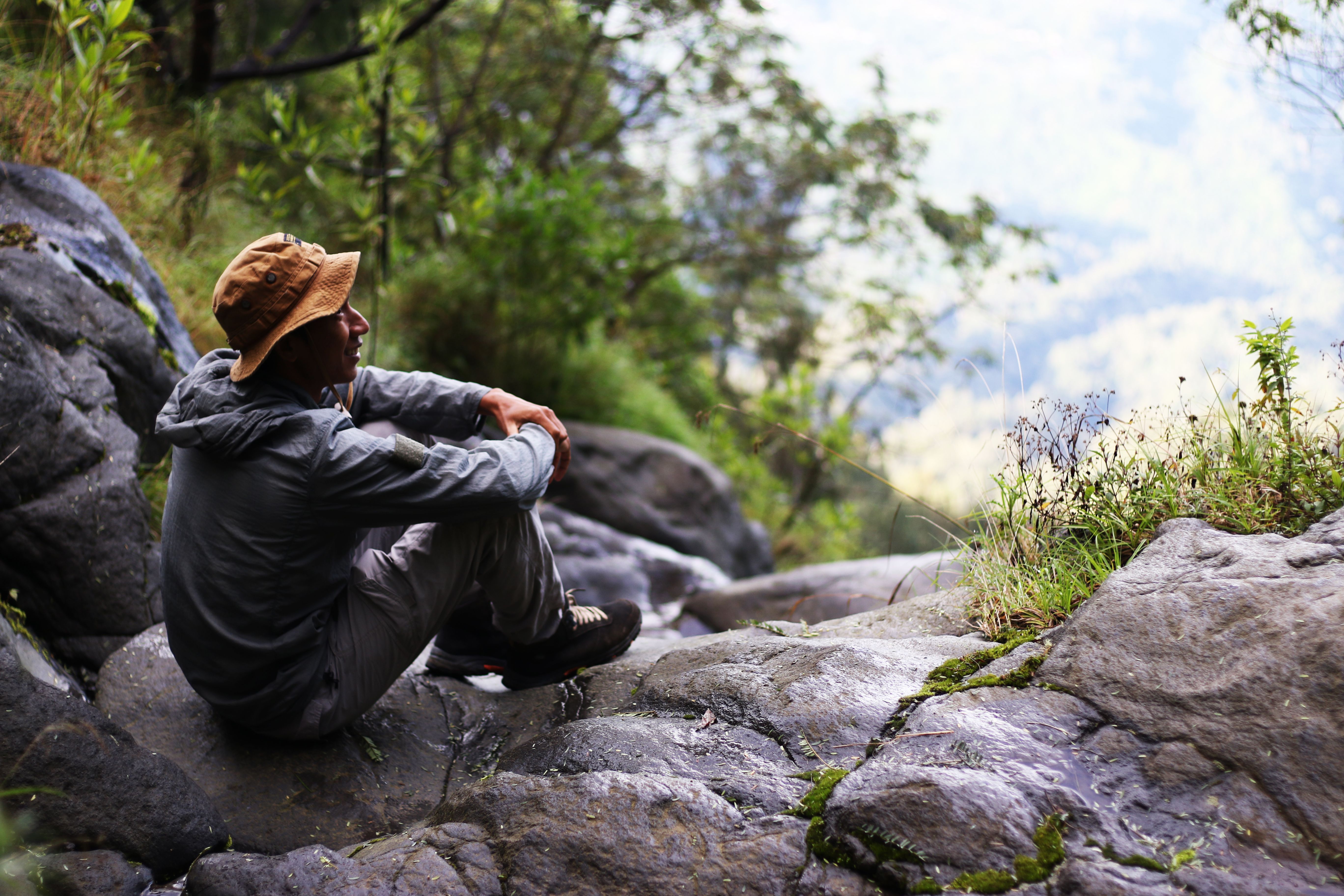 Man sitting peacefully on rocky terrain in Bali, surrounded by lush greenery and mountain views.