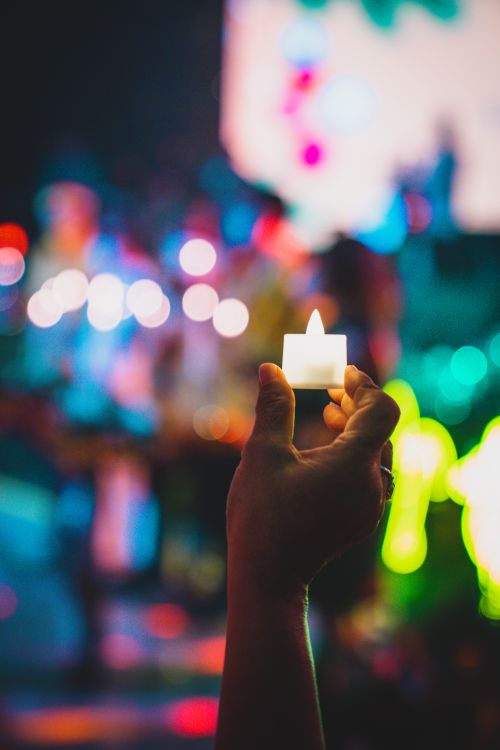 Free Silhouette of a hand holding a candle with colorful bokeh lights in the background, creating a vibrant atmosphere. Stock Photo