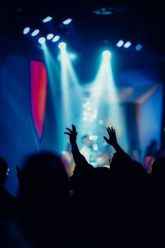 Silhouetted crowd with hands raised against colorful concert lights in Jakarta, Indonesia.